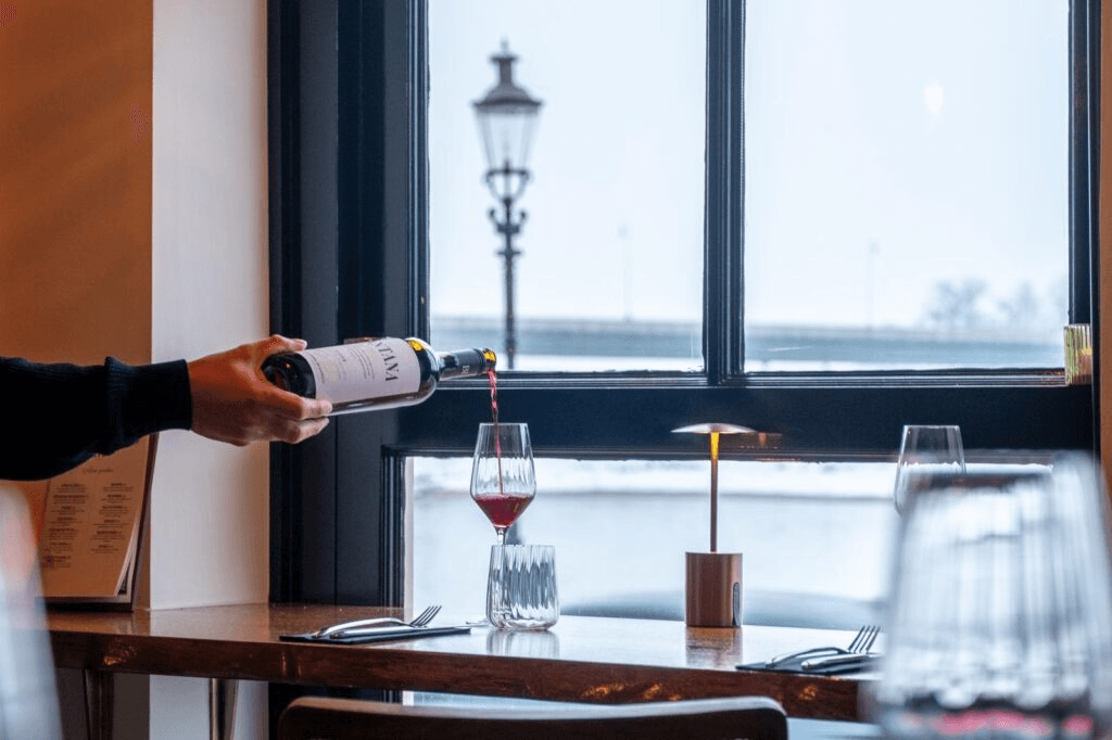 Rode wijn wordt ingeschonken aan een tafel met uitzicht op de IJssel